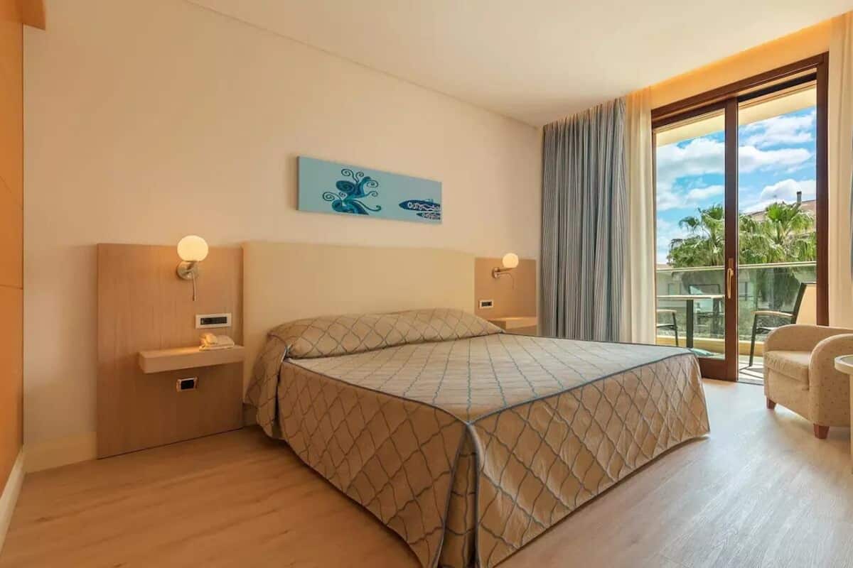 A hotel room with a bed, bedside tables, a nightstand, a window with curtains, and a view of the outdoors.