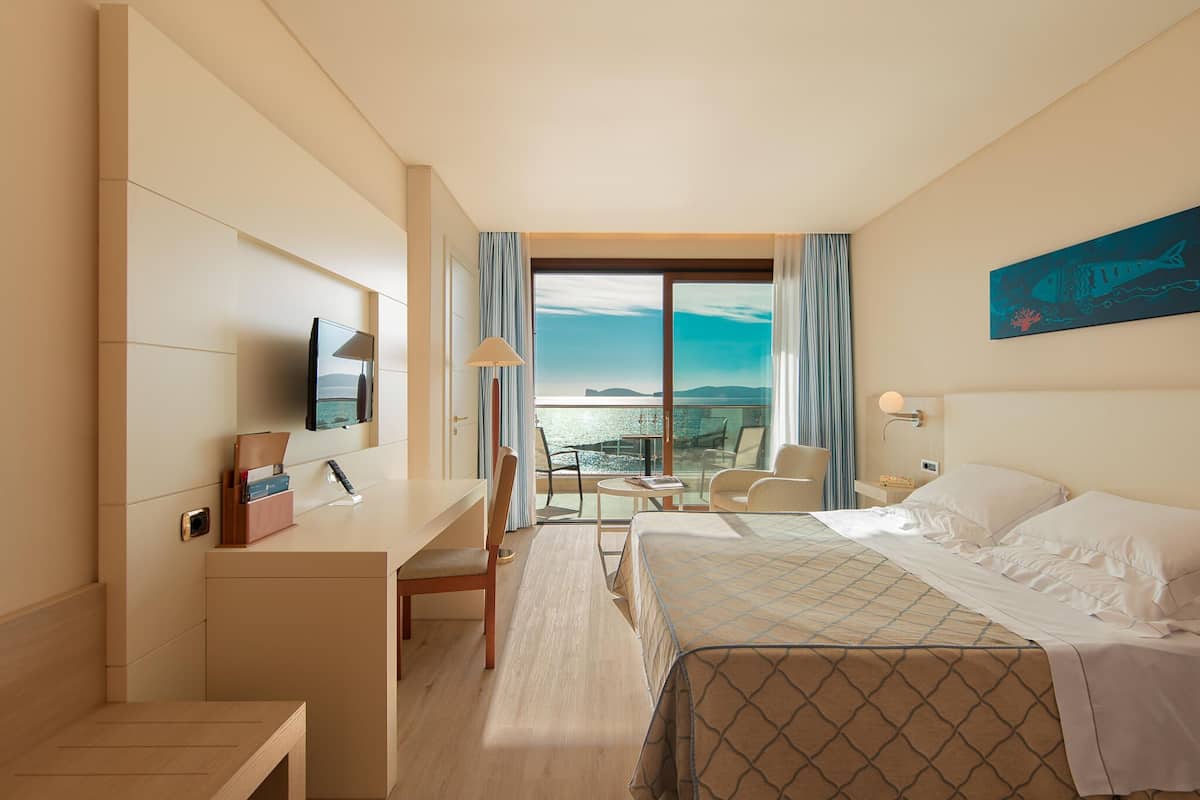 A hotel room with a bed, desk, chair, and a view of the sea.