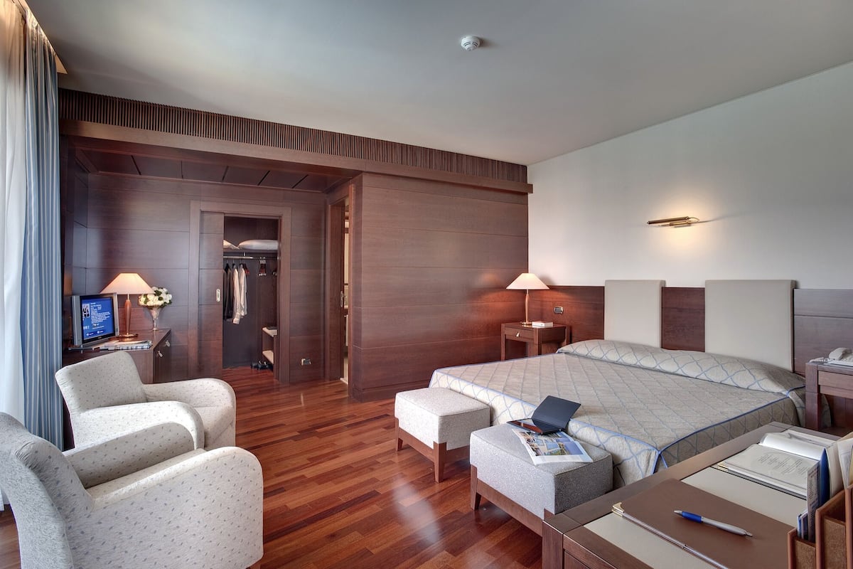 A hotel room with a large bed, two bedside tables, a desk with a chair, a wardrobe, and a television.