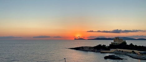 A coastal sunset view with a building on a small island.