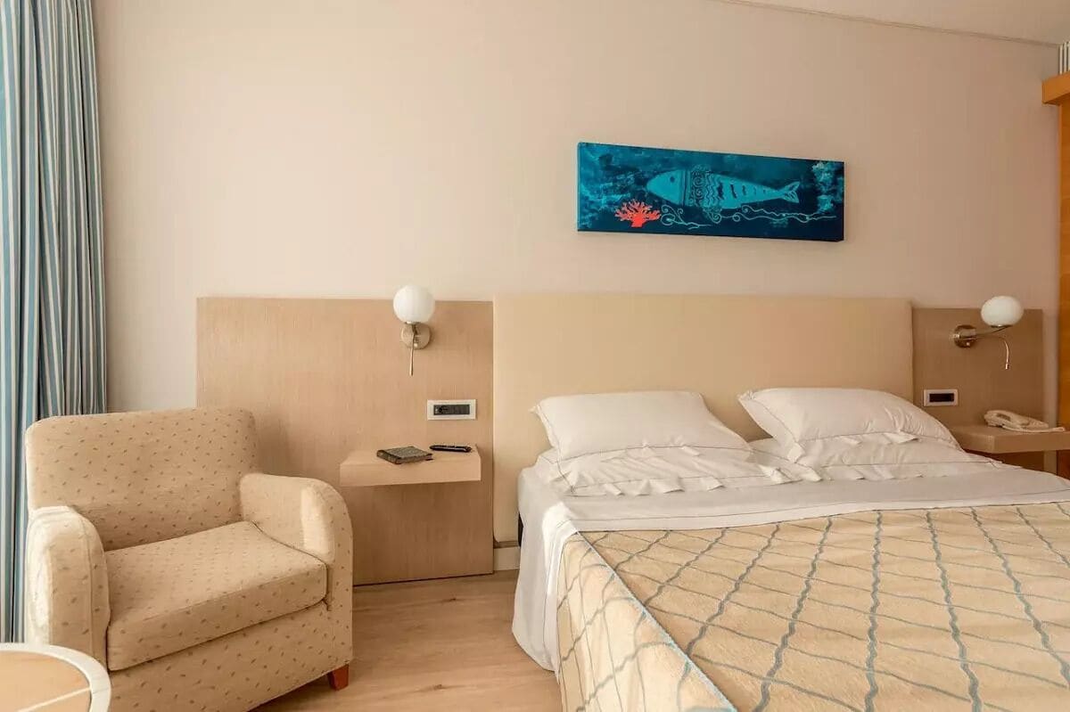 A hotel room with a bed, a chair, a nightstand, and a wall-mounted painting.