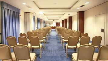 A hotel conference room with rows of beige chairs, a blue carpet, and a long corridor with curtains on the left.