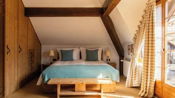 A bedroom with a wooden ceiling, a bed with white and teal bedding, a bedside table with lamps, and a window with curtains.