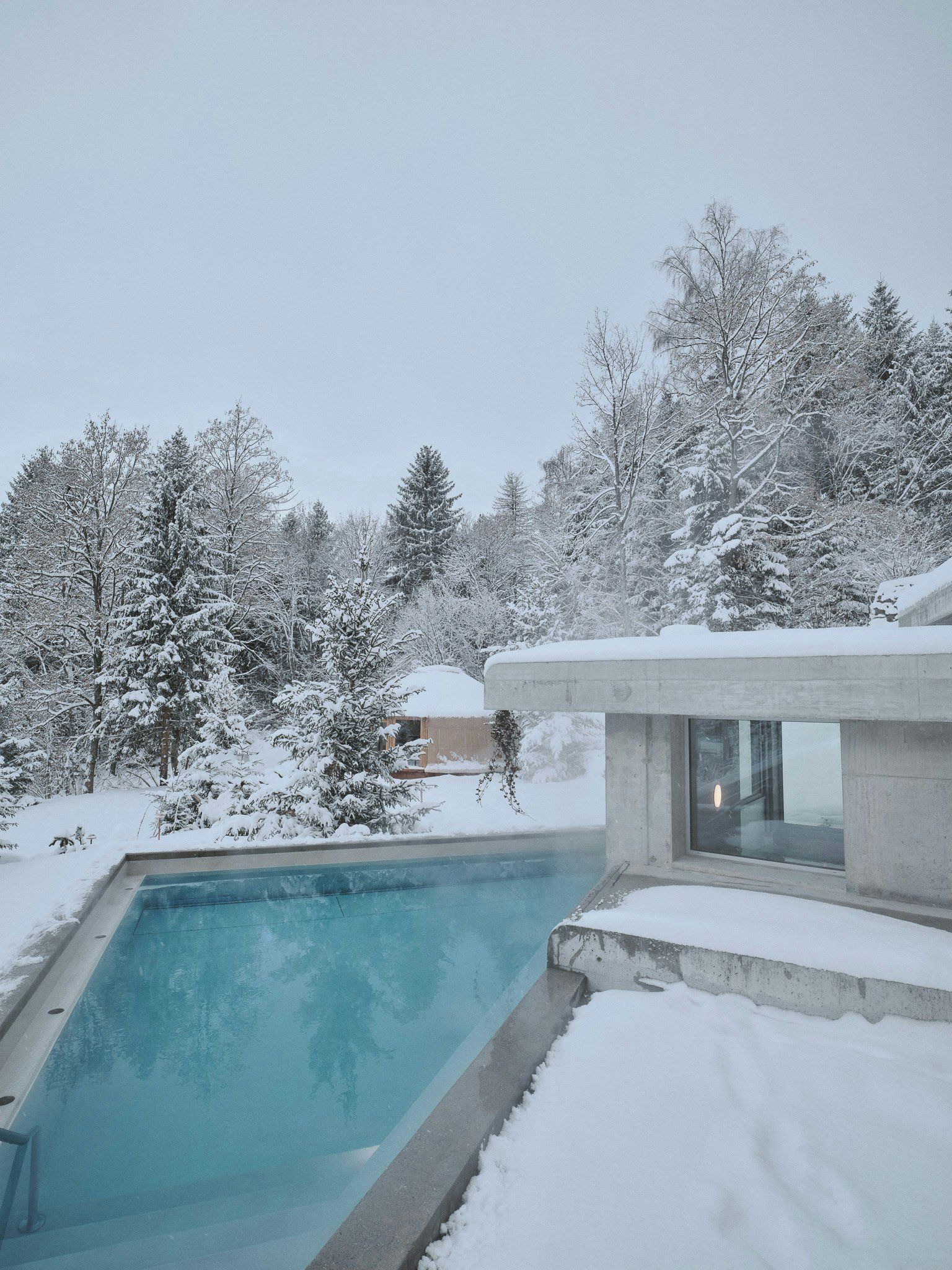 A swimming pool with a snow-covered deck and a modern building with large windows.