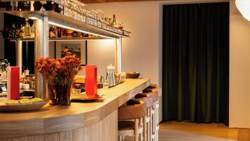 A bar area with a wooden counter, bar stools, a vase with flowers, and various bottles and glasses.