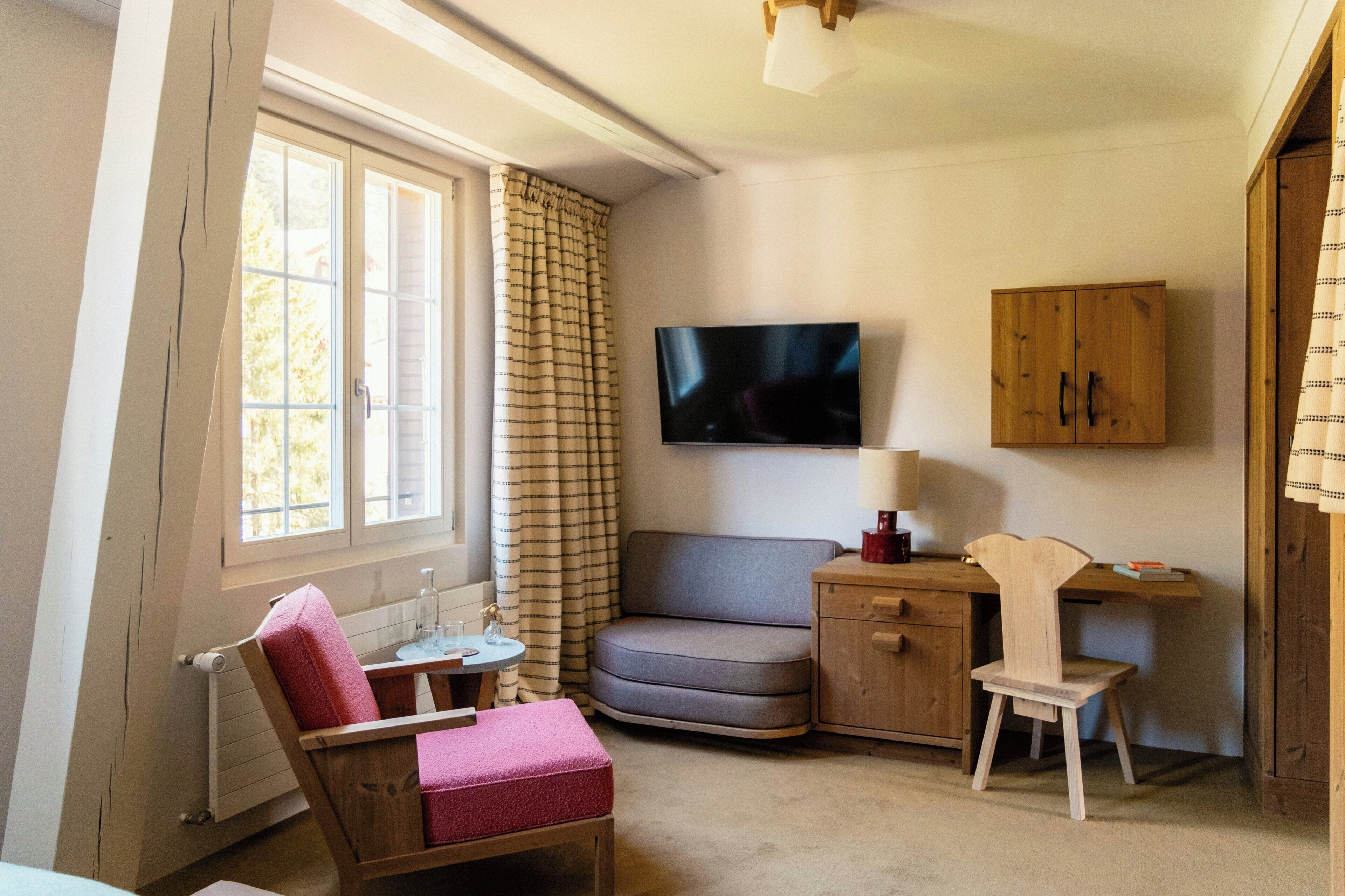 A room with a sofa, a wooden chair, a small table, a TV, and a cabinet.