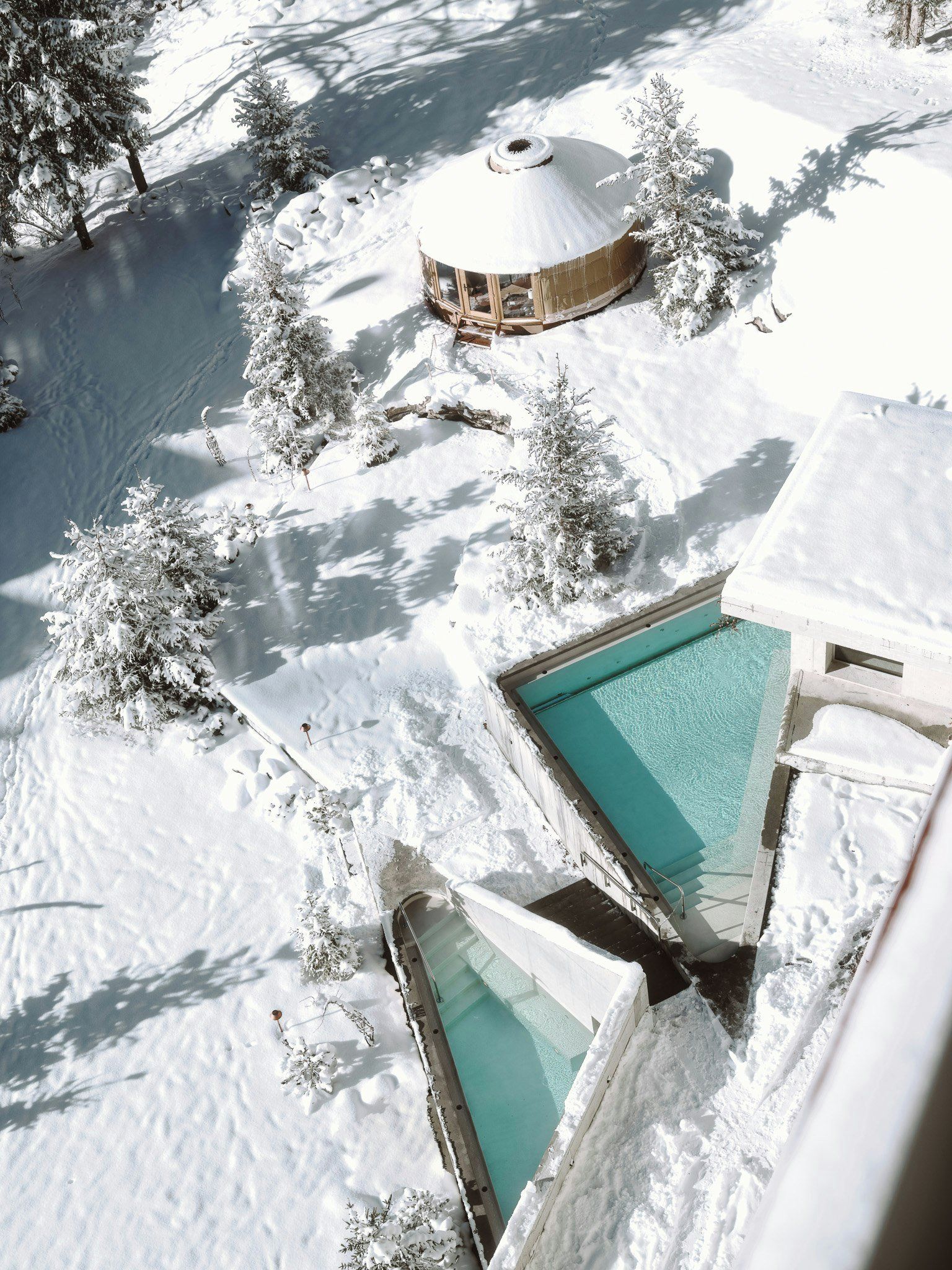 Ein verschneiter Außenbereich mit Pool, einem hölzernen Pavillon und schneebedeckten Bäumen.
