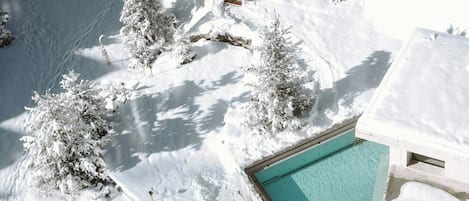 Un espacio exterior cubierto de nieve con una piscina, un pabellón de madera y árboles cargados de nieve.