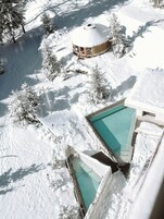 Un espacio exterior cubierto de nieve con una piscina, un pabellón de madera y árboles cargados de nieve.