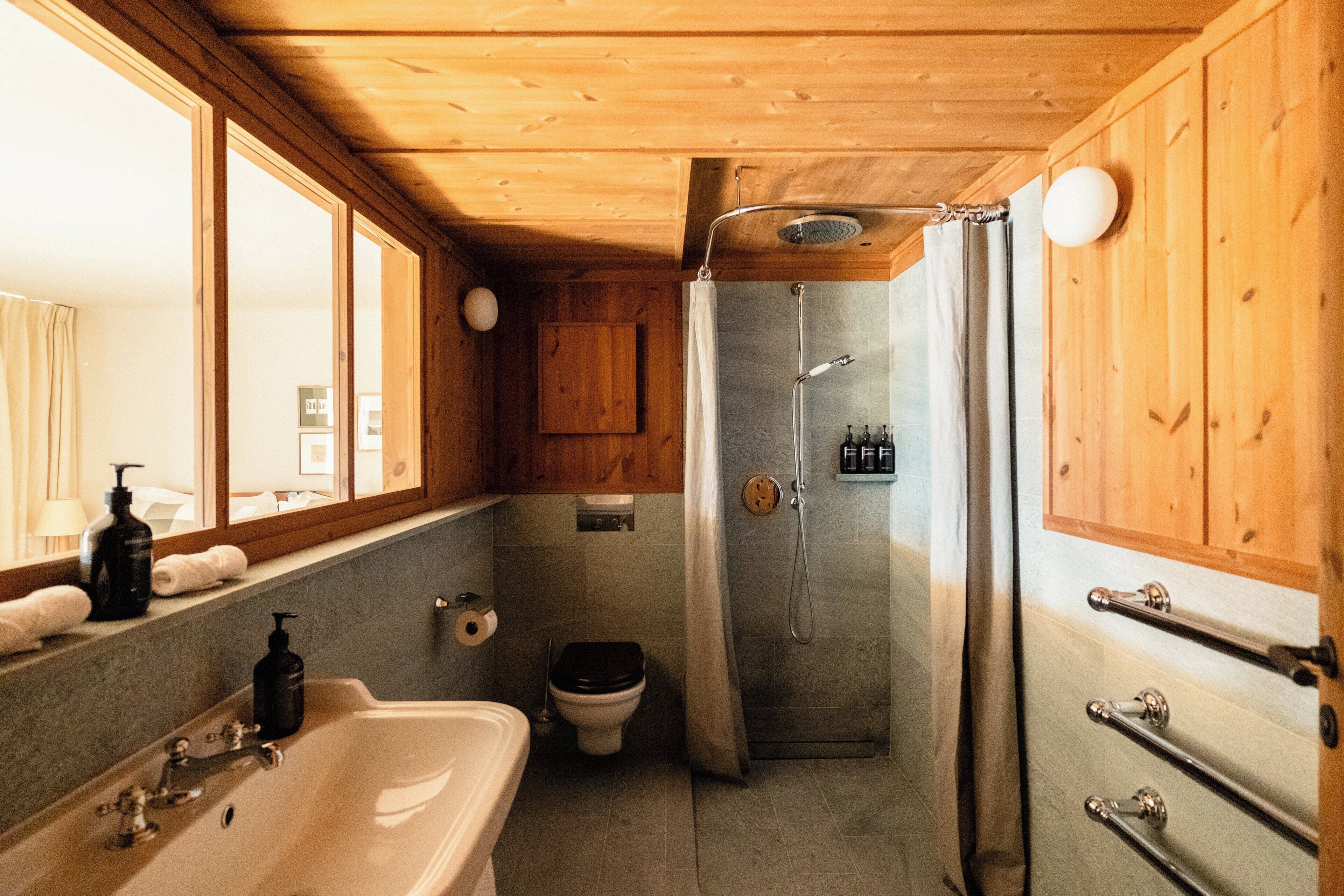 A bathroom with a bathtub, toilet, shower, wooden walls, and a window.