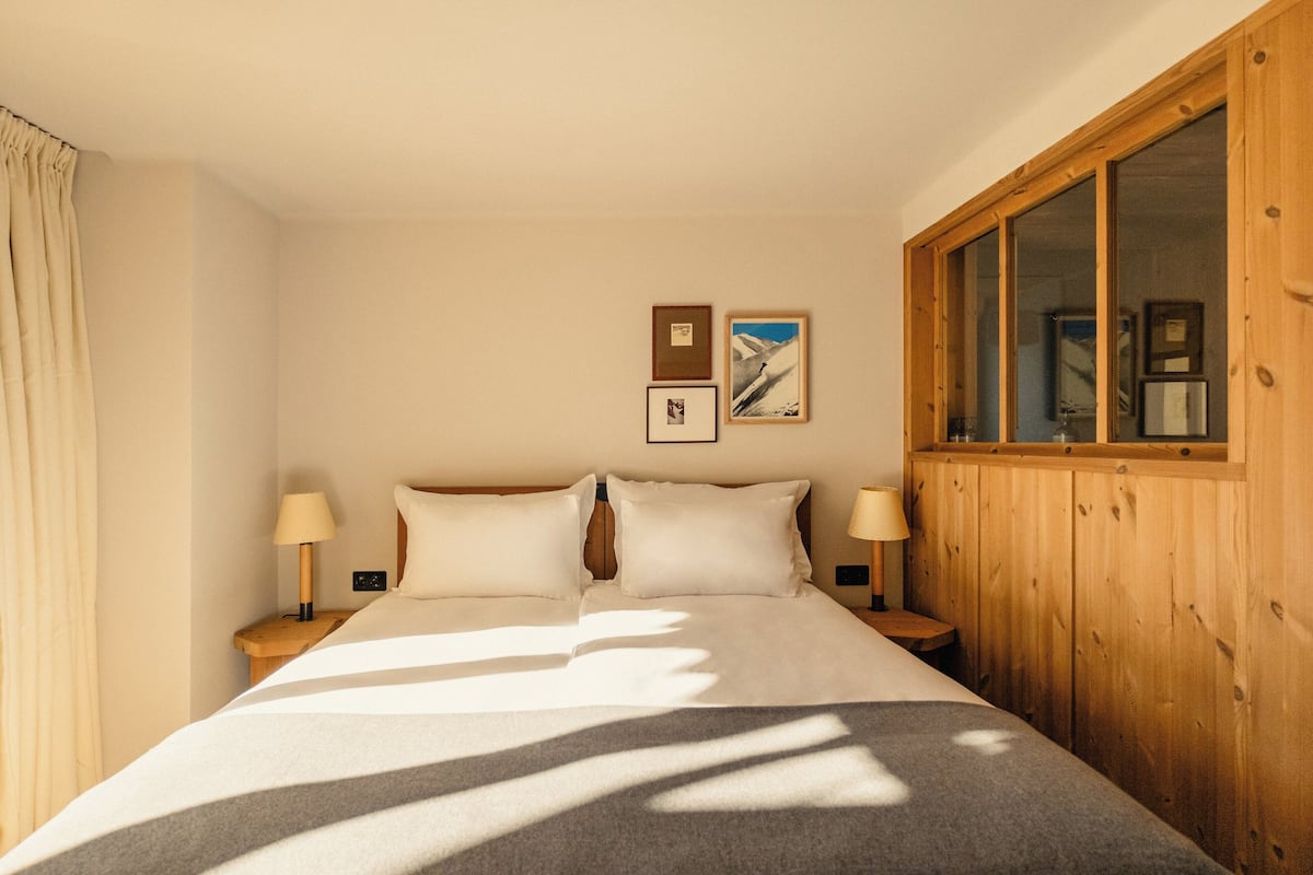 Une chambre avec un grand lit, deux tables de chevet avec des lampes, un lambris en bois sur les murs et deux tableaux encadrés accrochés au mur.