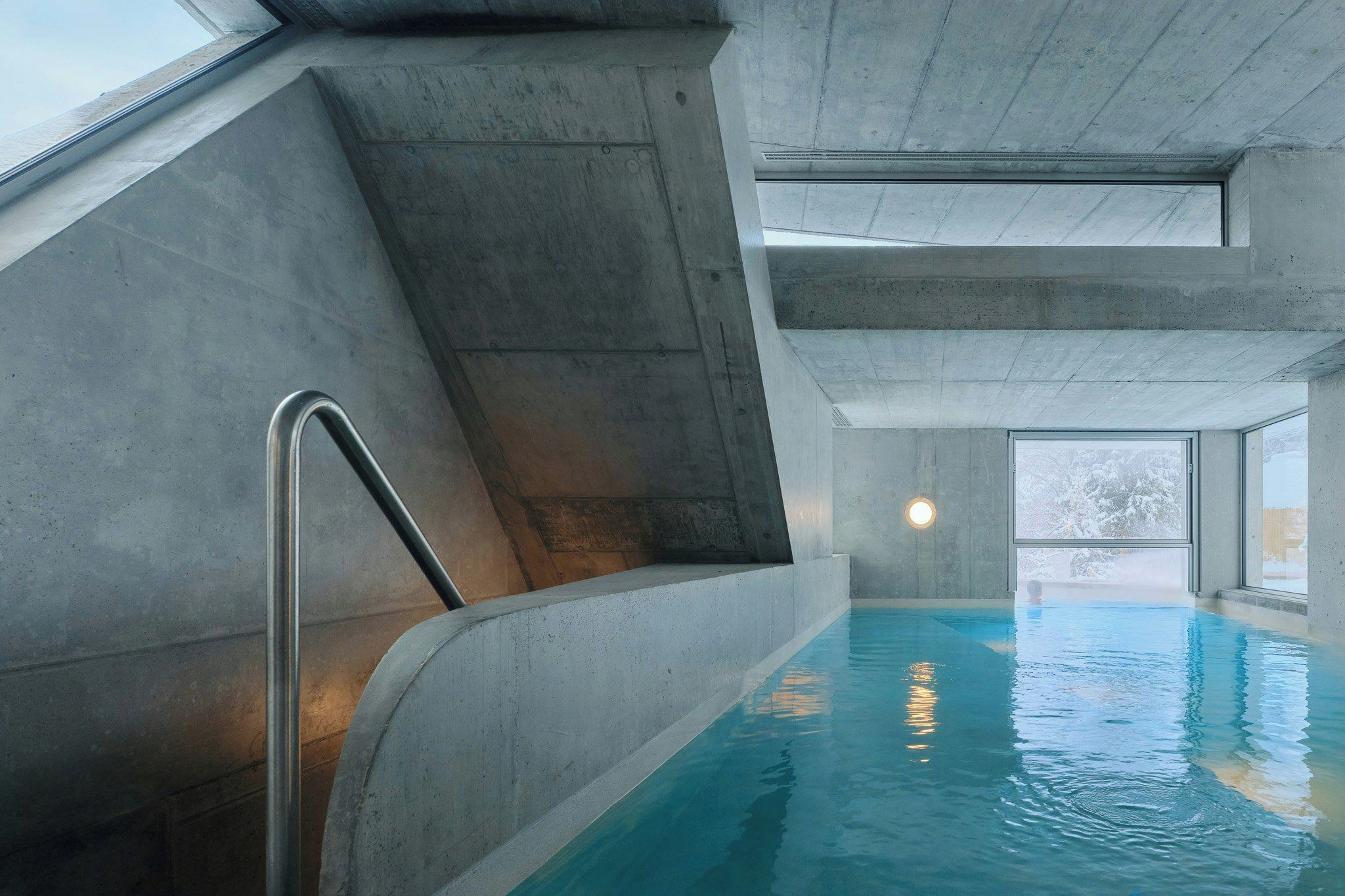 Ein überdachter Pool mit Betonwänden, einer Metallleiter und einem Fenster mit Blick nach draußen.
