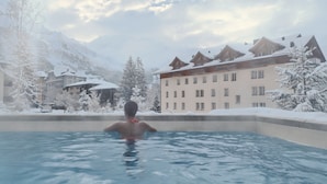Una persona en una piscina con árboles y edificios cubiertos de nieve al fondo.