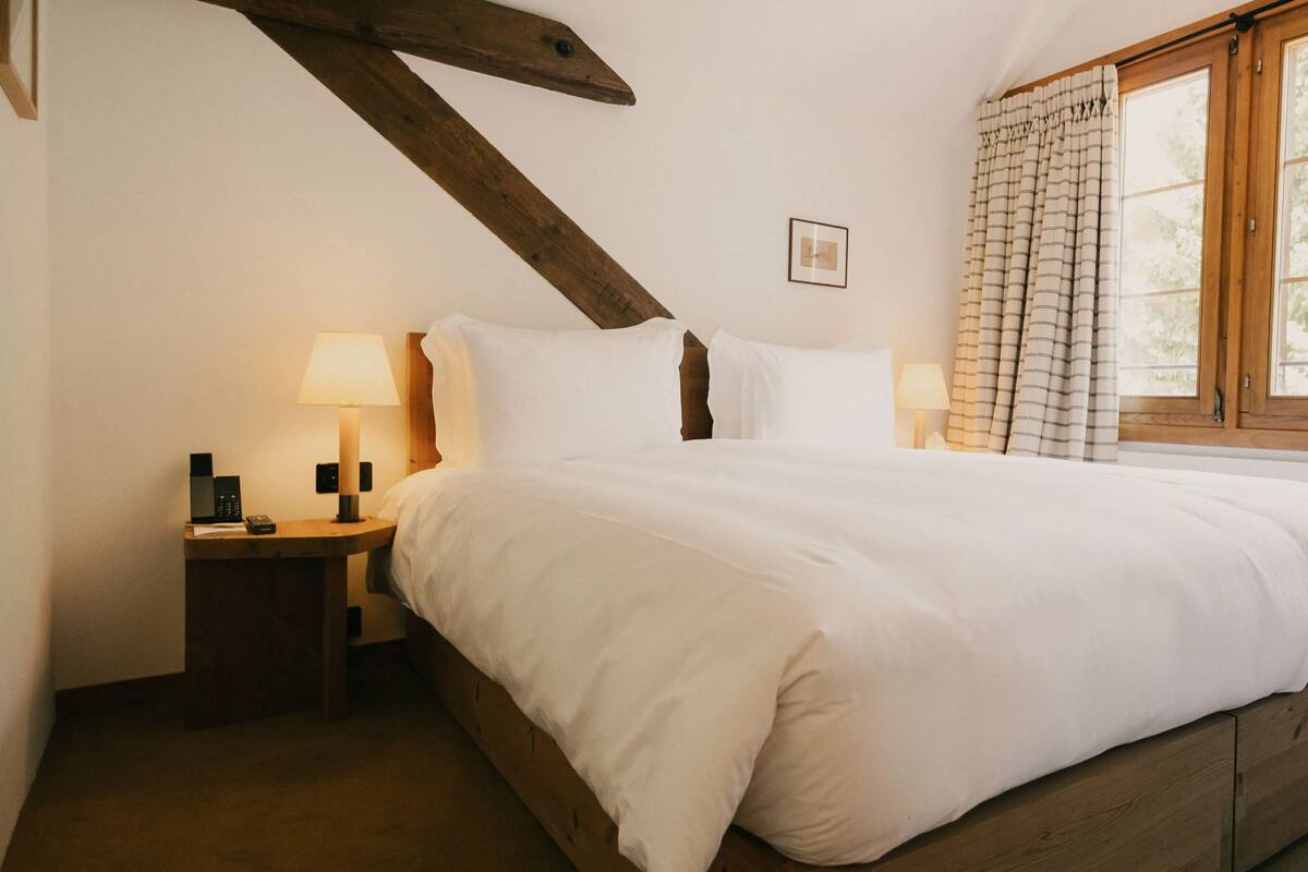 Une chambre à coucher avec un lit en bois, une table de chevet avec une lampe, une fenêtre avec des rideaux et un tableau encadré au mur.