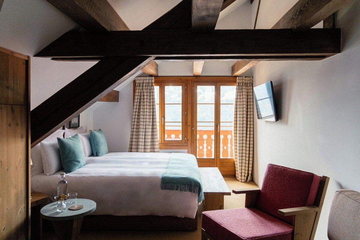 Une chambre à coucher avec un lit, une table de chevet, une chaise, un téléviseur et une fenêtre avec des rideaux.