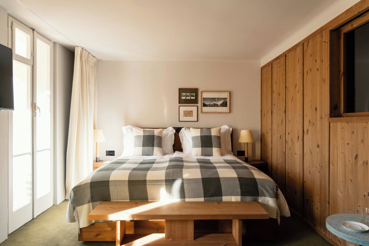 Une chambre à coucher avec un lit, des lampes de chevet, un banc en bois, une fenêtre et un mur orné de tableaux.