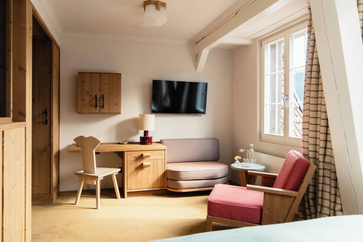Une pièce comprenant un lit, un bureau, une chaise, un canapé, une télévision et une fenêtre avec des rideaux.