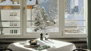 Un comedor con una mesa para dos, una ventana con vistas a una montaña nevada y un edificio de estilo arquitectónico tradicional.