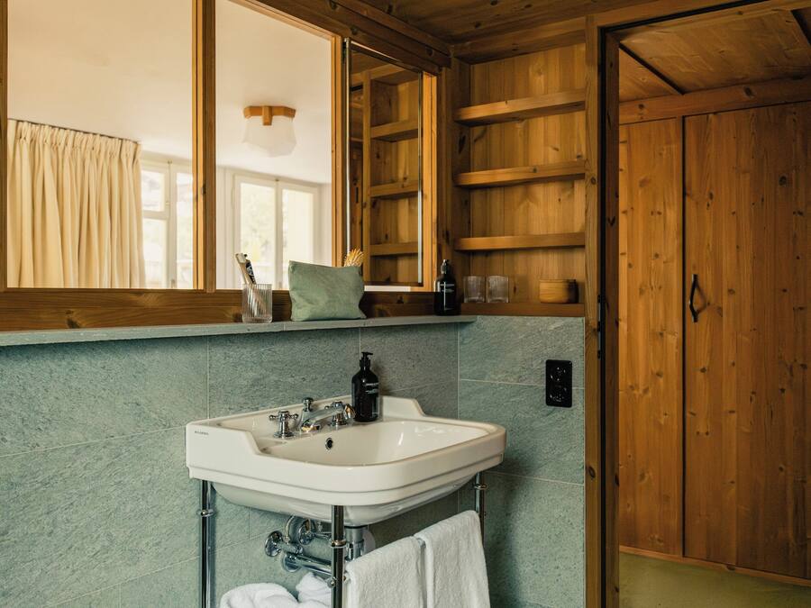 Un baño con lavamanos blanco, armarios de madera y un espejo grande.