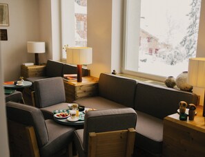 A cozy room with a sofa, chairs, a small table with food and drinks, a lamp, and a window with a view of snow outside.