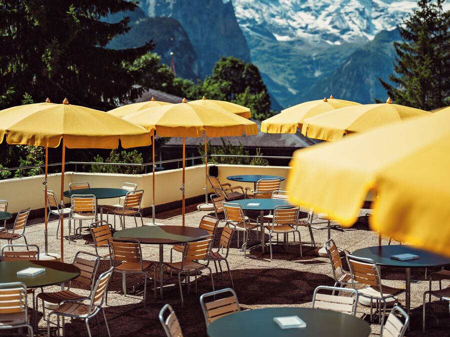 Outdoor seating with yellow umbrellas, tables, and chairs, set against a mountainous backdrop.
