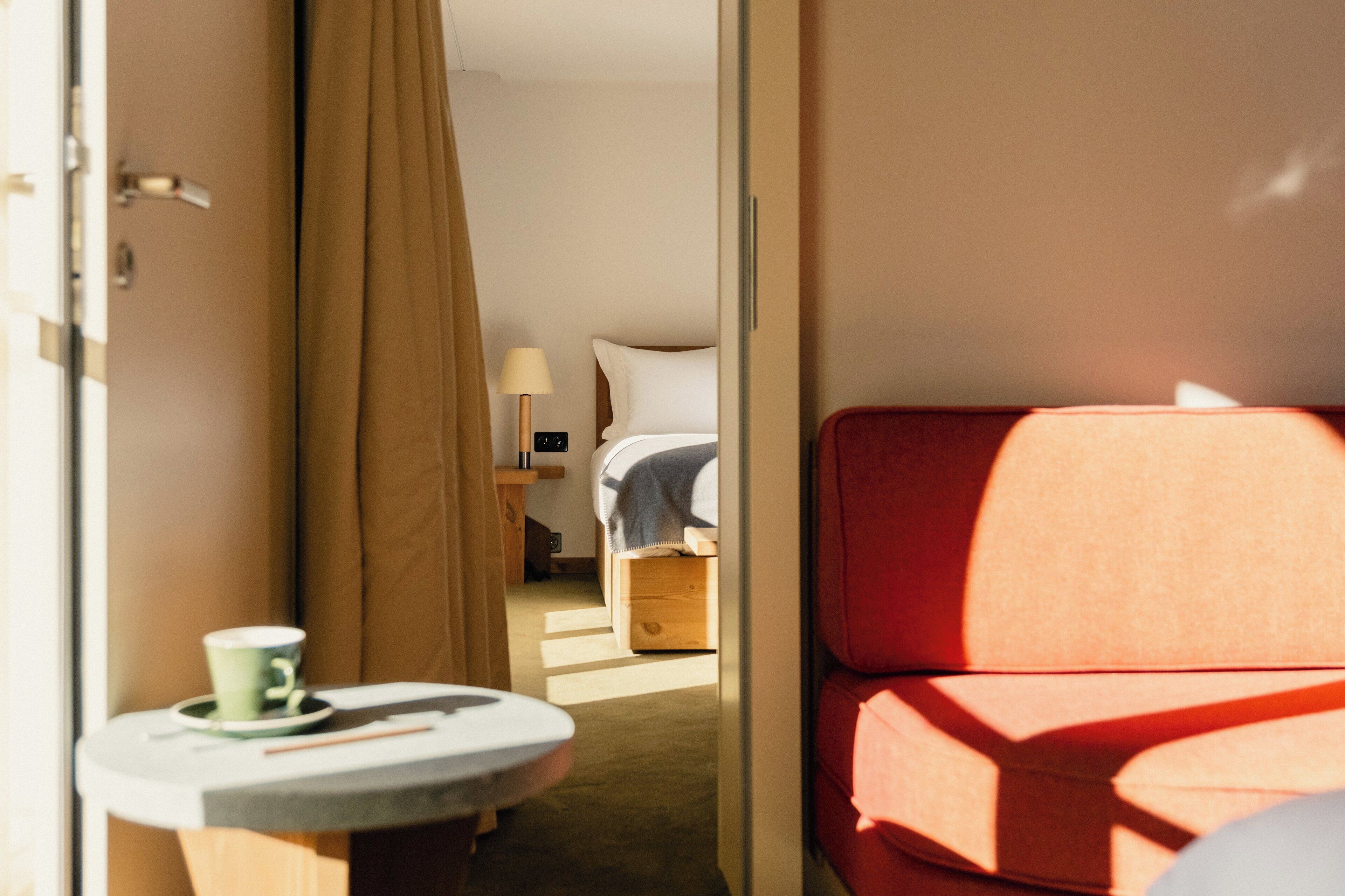 A hotel room with a bed, a small table with a cup, and a red chair.