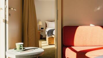 A hotel room with a bed, a small table with a cup, and a red chair.