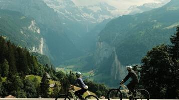 Two cyclists on a paved path with a mountainous landscape in the background.