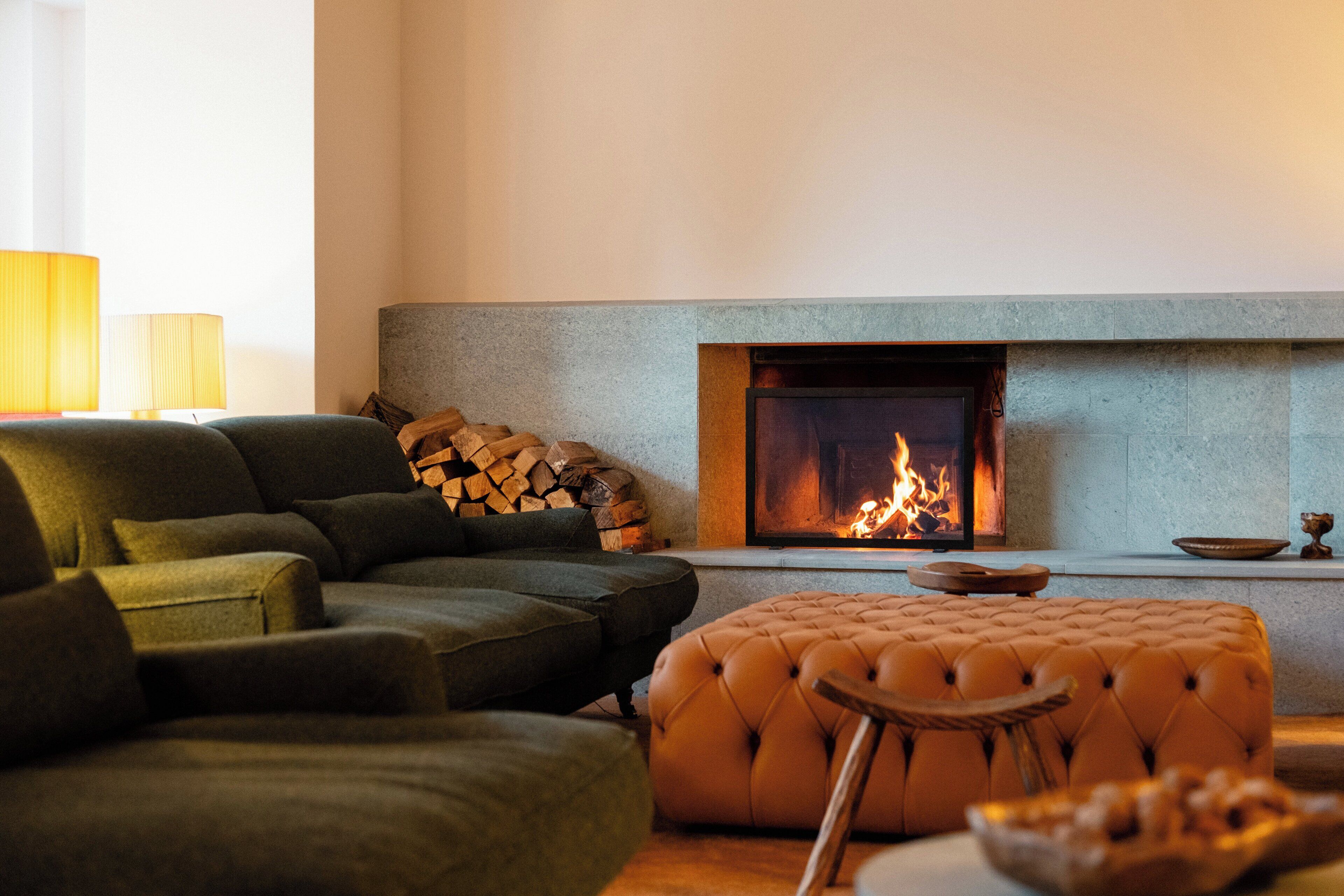 A cozy living room with a fireplace, a green sofa, and a tufted ottoman.