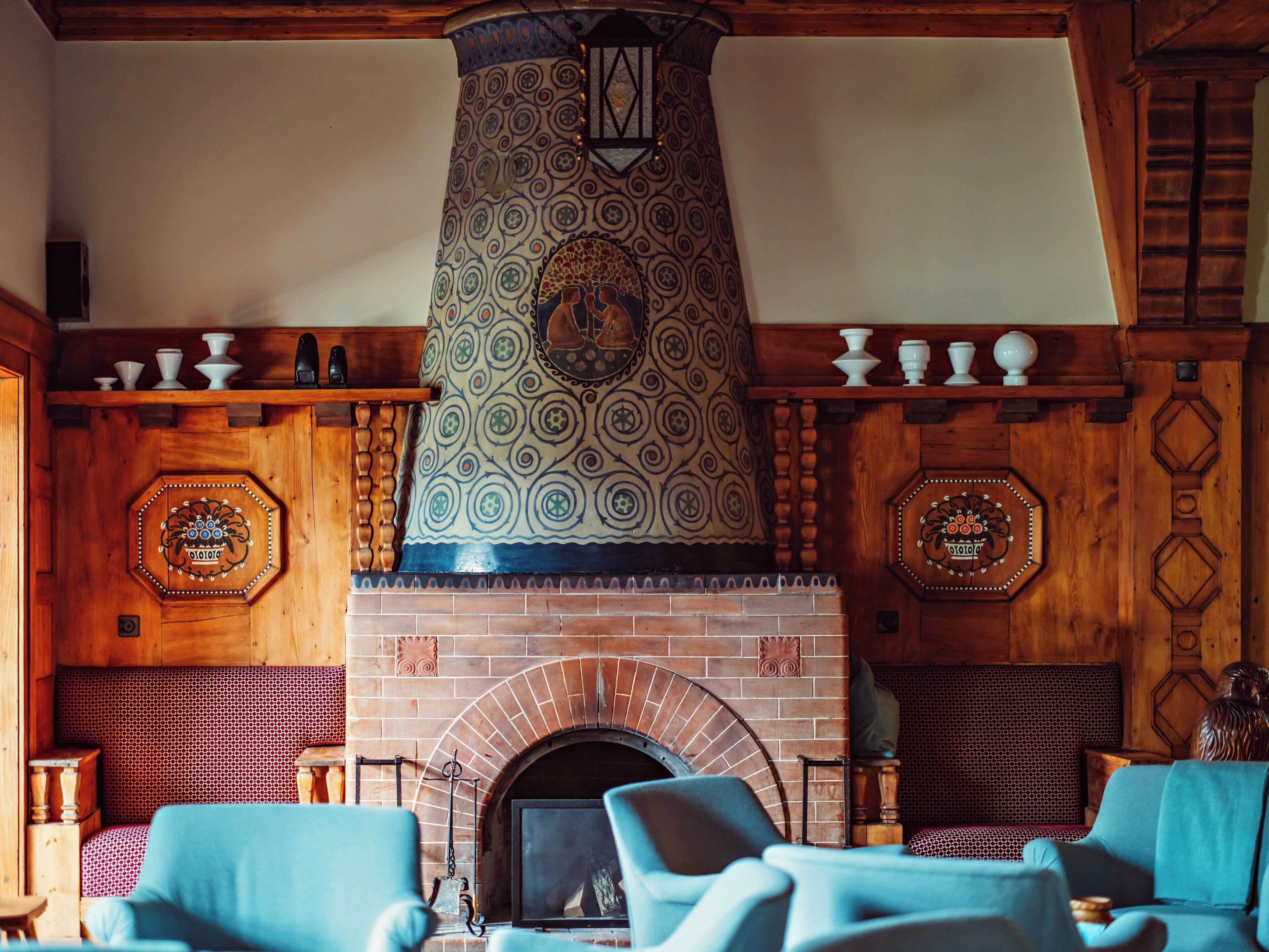 A cozy room with a brick fireplace, patterned wall tiles, and wooden beams.