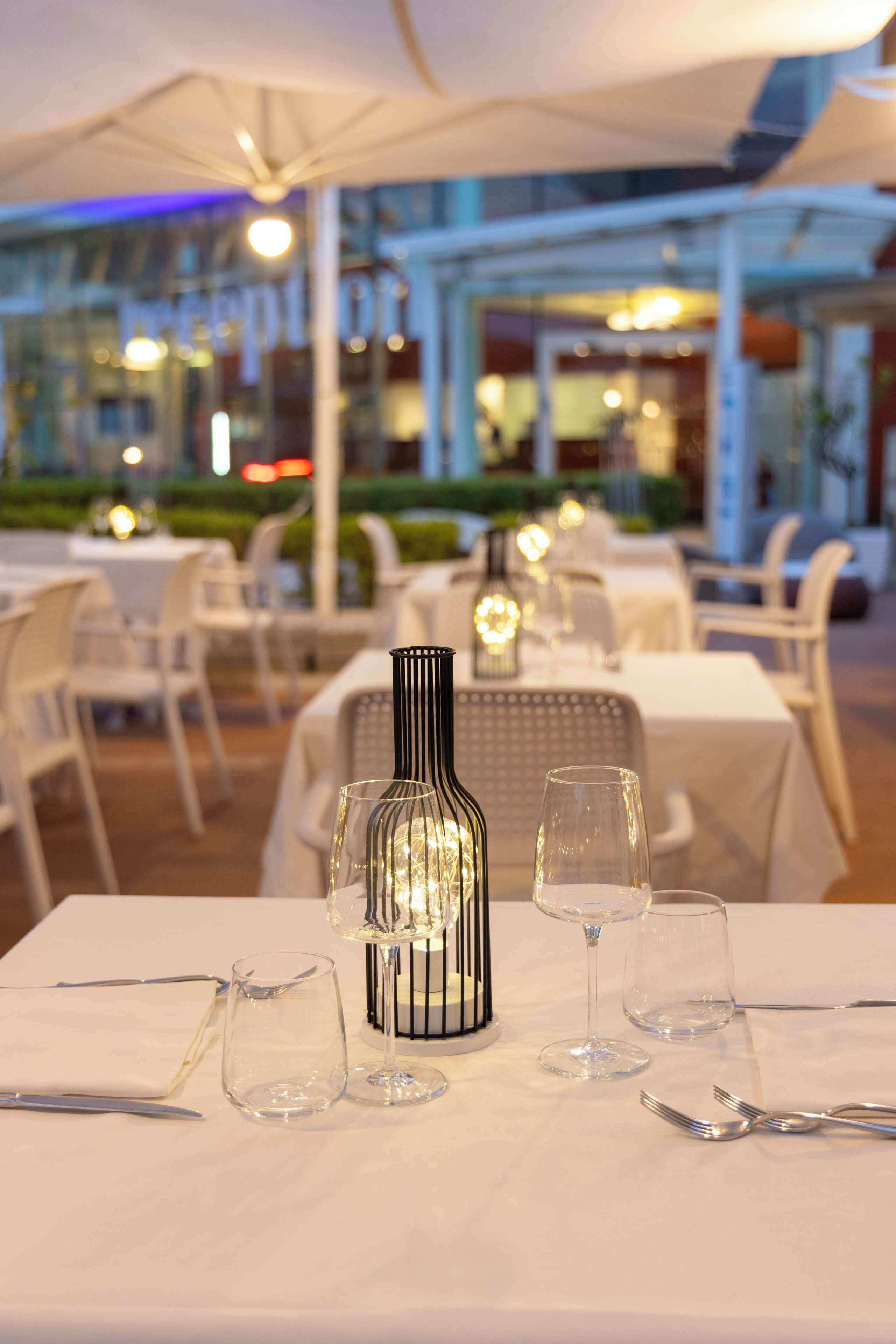 A dining area with tables set for two, featuring white tablecloths and a decorative bottle centerpiece.