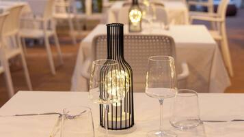 Un espace repas avec des tables préparées pour deux personnes, agrémenté de nappes blanches et d’une bouteille décorative servant de centre de table.