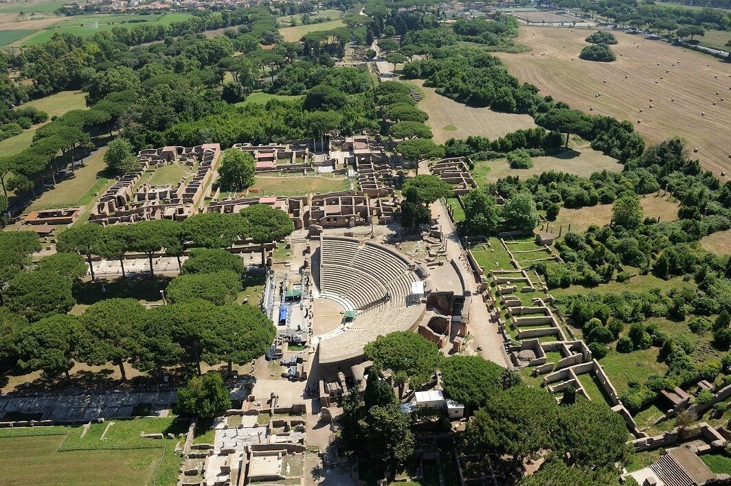 Una vista aerea di un antico anfiteatro circondato da vegetazione lussureggiante e campi.