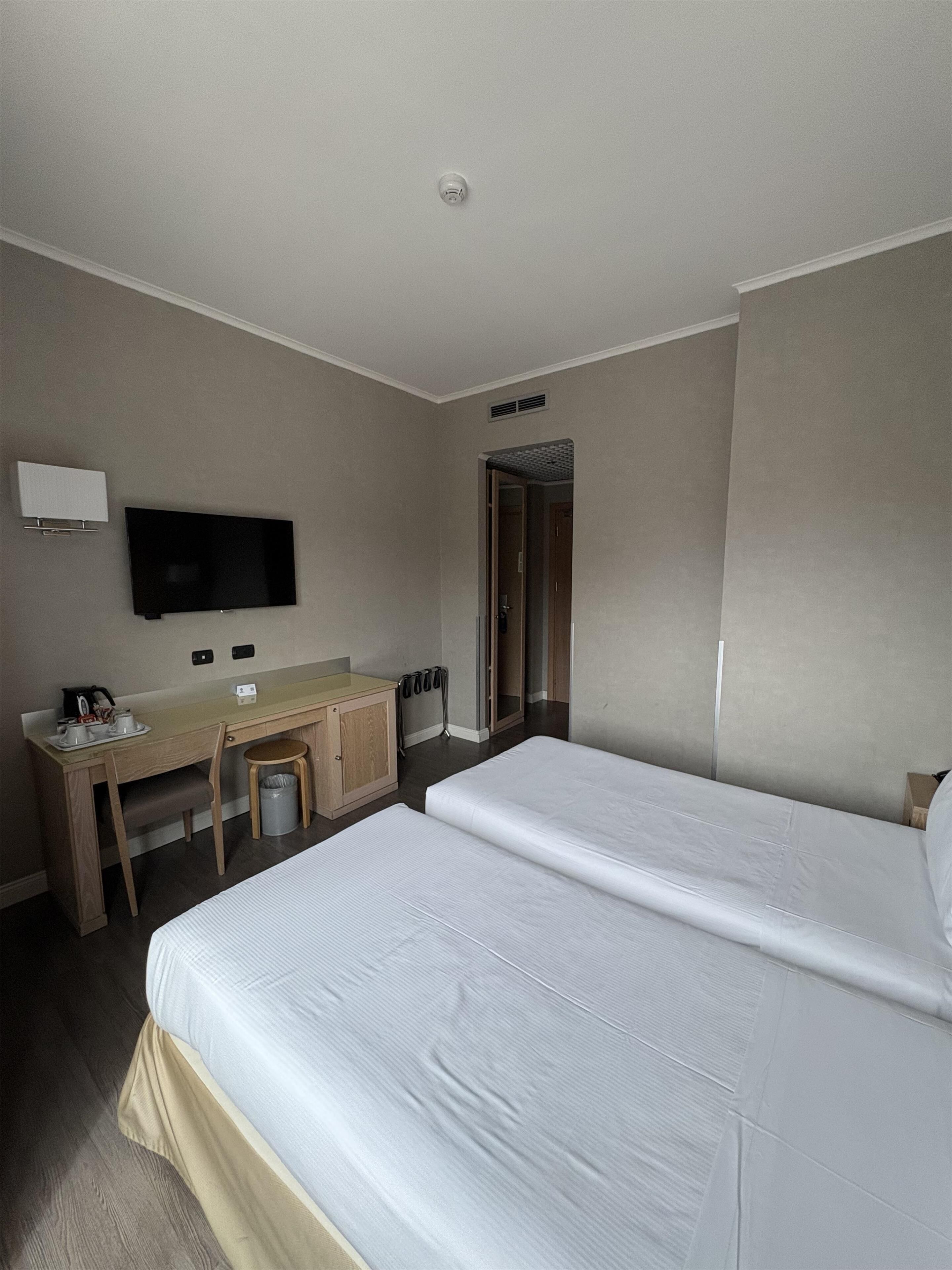 A hotel room with two beds, a desk, a chair, a television, and a trash can.