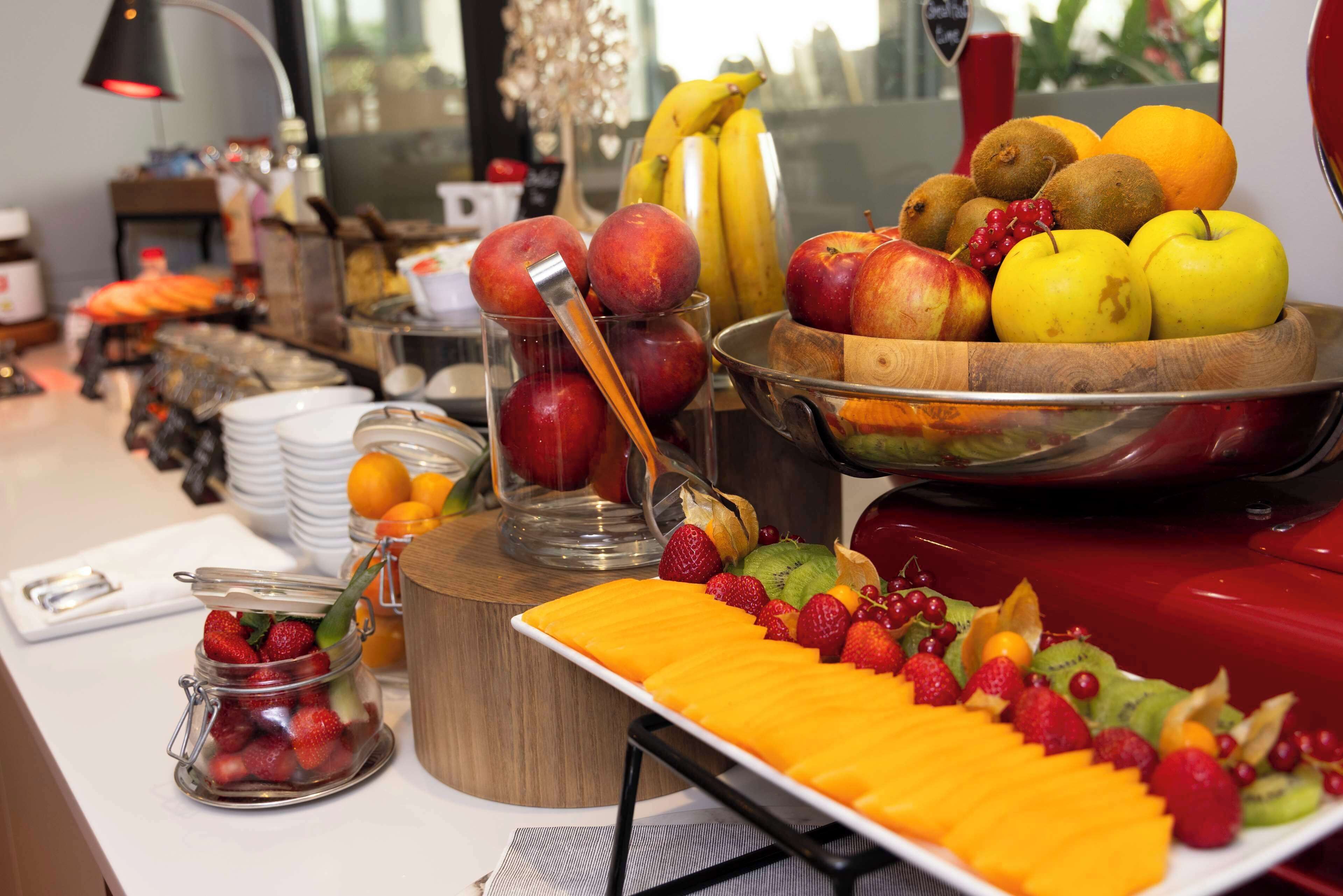 A buffet table with various fruits and a glass jar of strawberries.