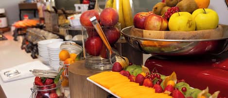 A buffet table with various fruits and a glass jar of strawberries.