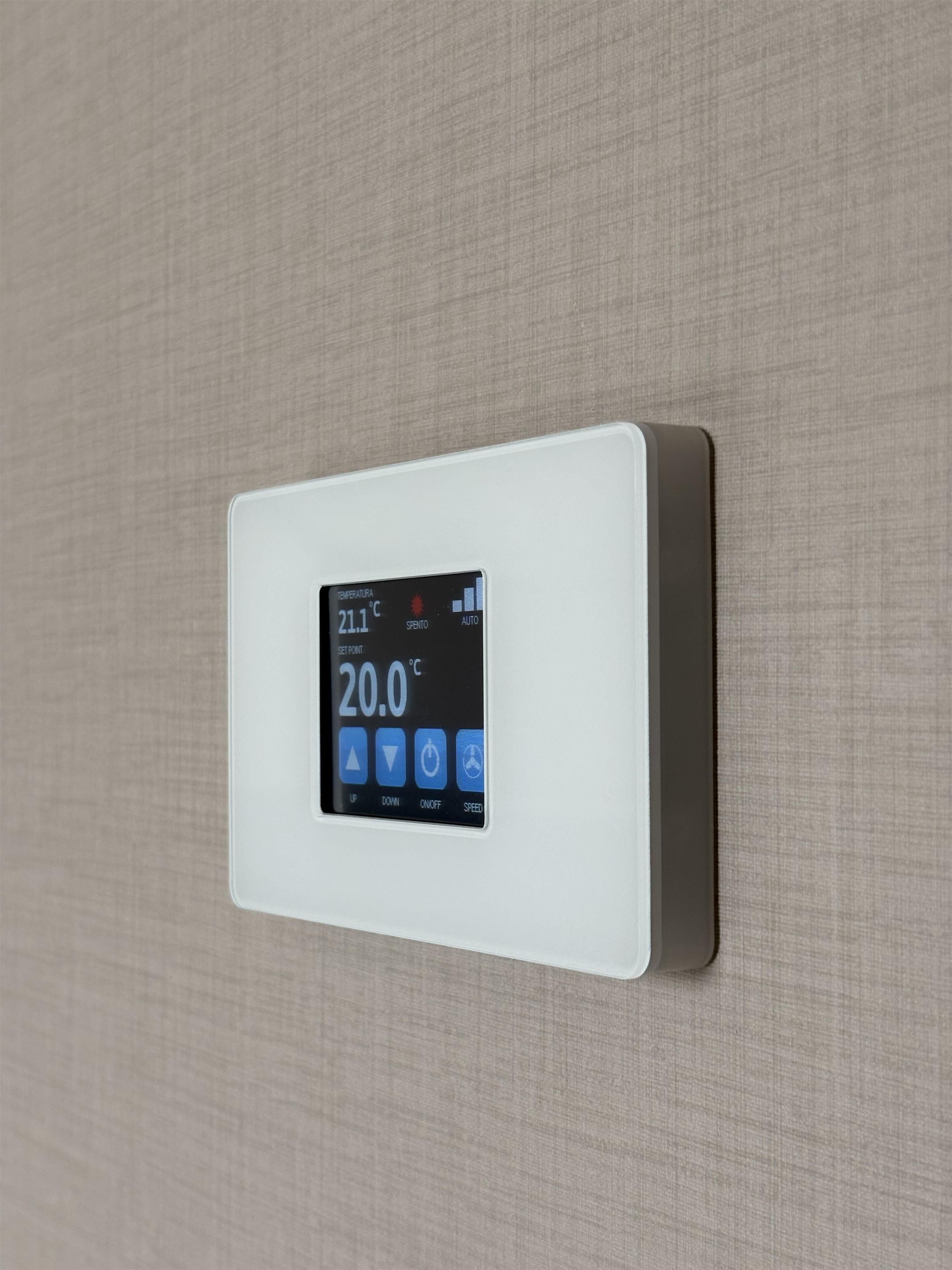 Termostato empotrado en la pared que muestra una temperatura de 21,1°C y un ajuste de 20,0°C, con cuatro botones de control etiquetados como SUBIR, BAJAR, ENCENDIDO/APAGADO y VELOCIDAD.