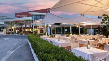 Un espace extérieur aménagé avec des tables et des parasols, situé à l’aéroport de Rome.