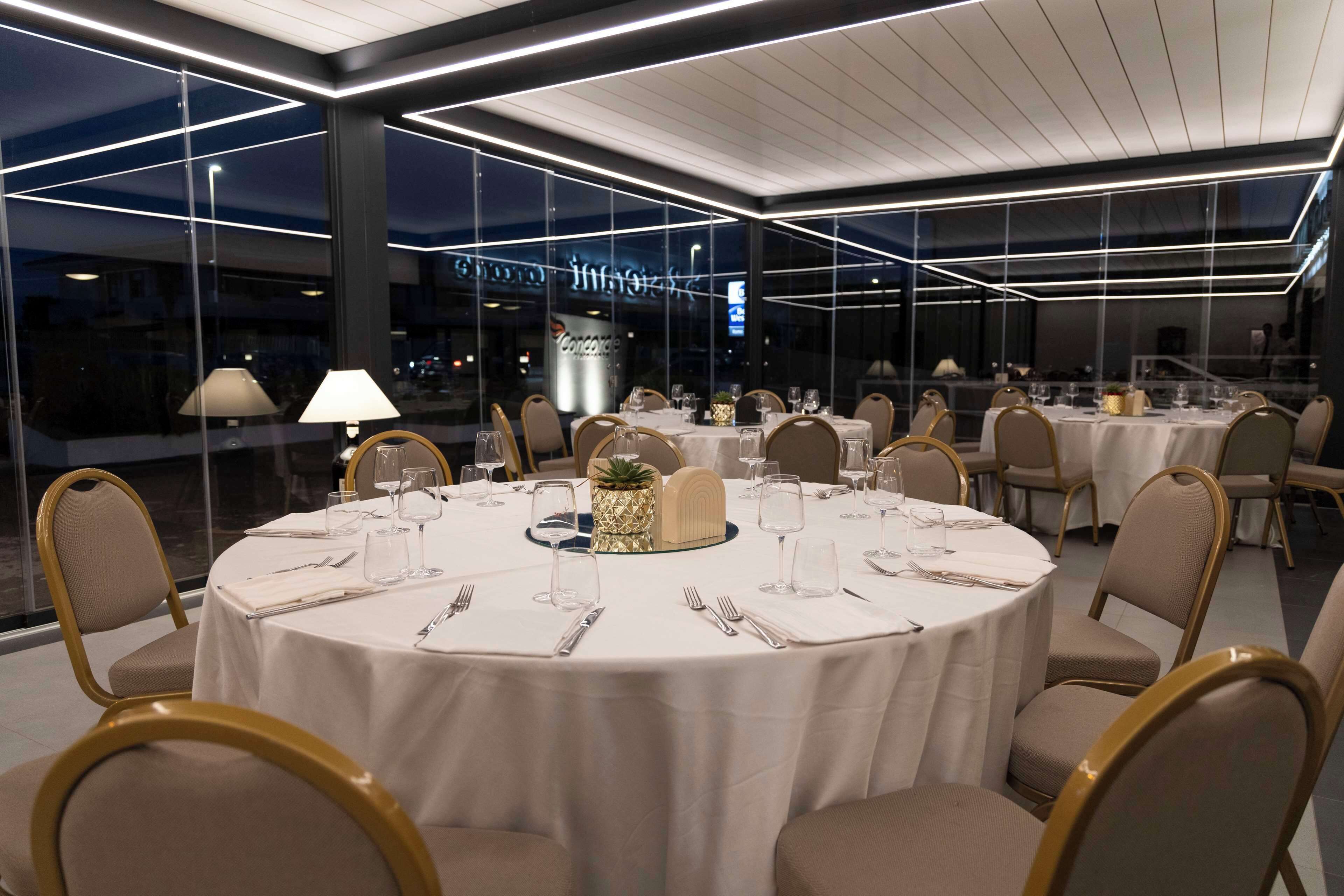 Un restaurante con mesas redondas dispuestas para comer, amplios ventanales y una decoración de diseño moderno.