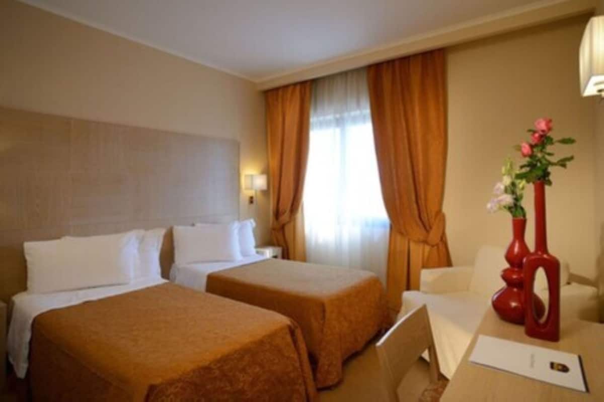 A hotel room with two beds, a desk, a chair, and a vase with flowers.