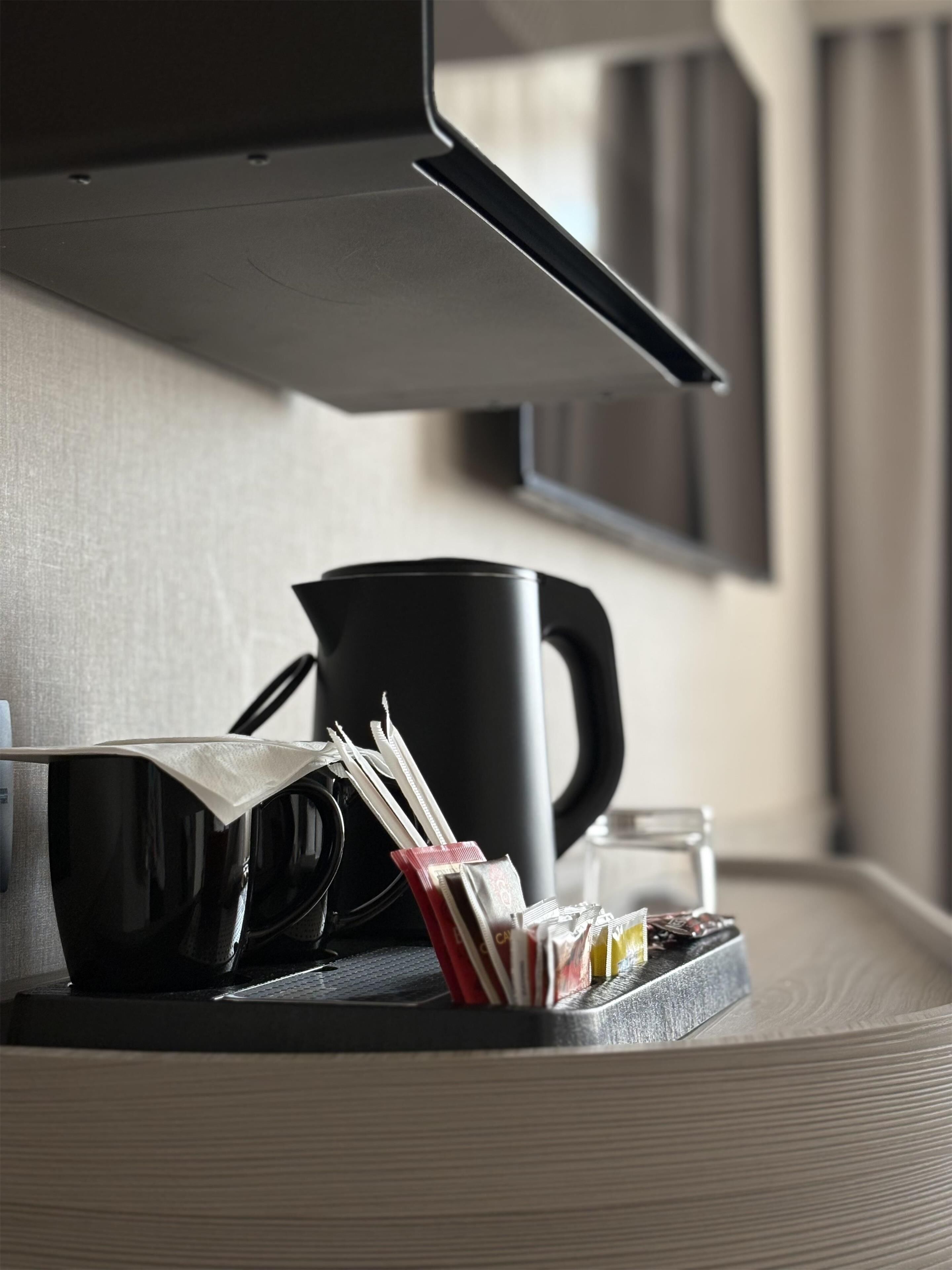 Una zona de cocina con una cafetera, una taza y una bandeja con cápsulas de café.