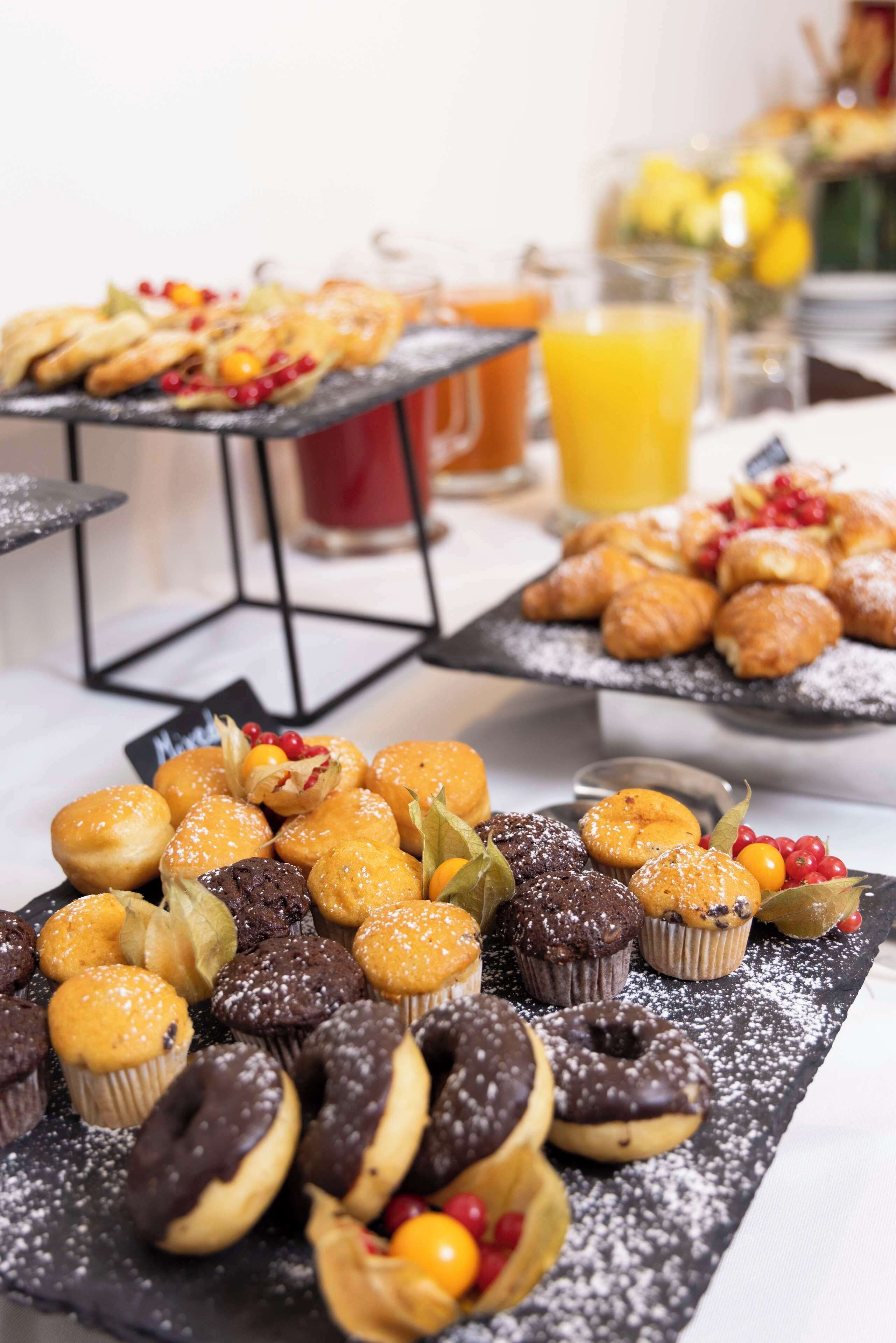 Un buffet con diversi dolci e pasticcini, tra cui muffin e ciambelle, disposti su vassoi neri.