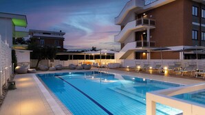 Una piscina amb gandules i ombrelles, envoltada d'edificis amb balcons i zones d'estar a l'aire lliure.