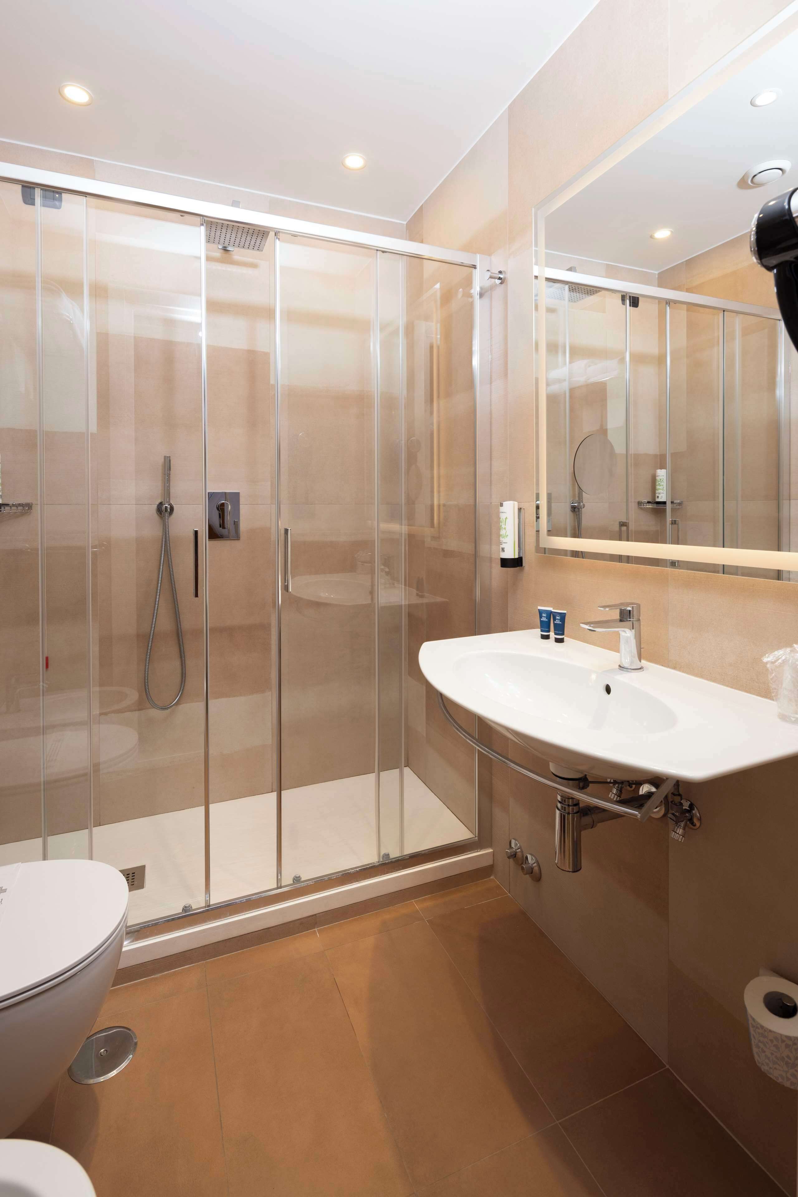 A modern bathroom with a glass-enclosed shower, a white sink, and a large mirror.