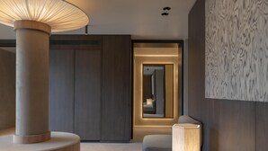 Habitació d'hotel moderna amb una taula rodona de fusta, una làmpada de peu, un sofà i un mirall gran.