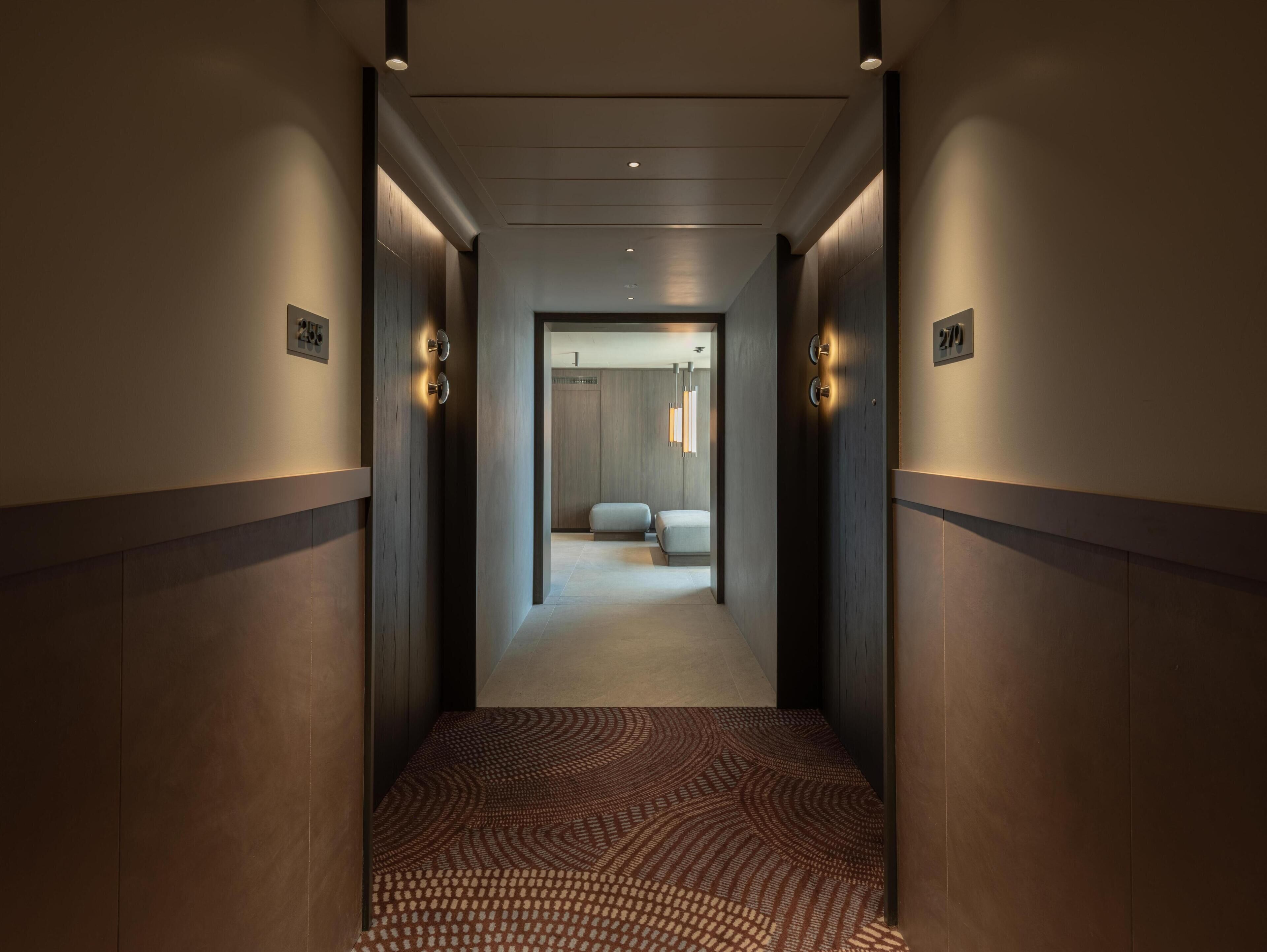 A hallway with a patterned carpet, a bed, and a door with a number plate.