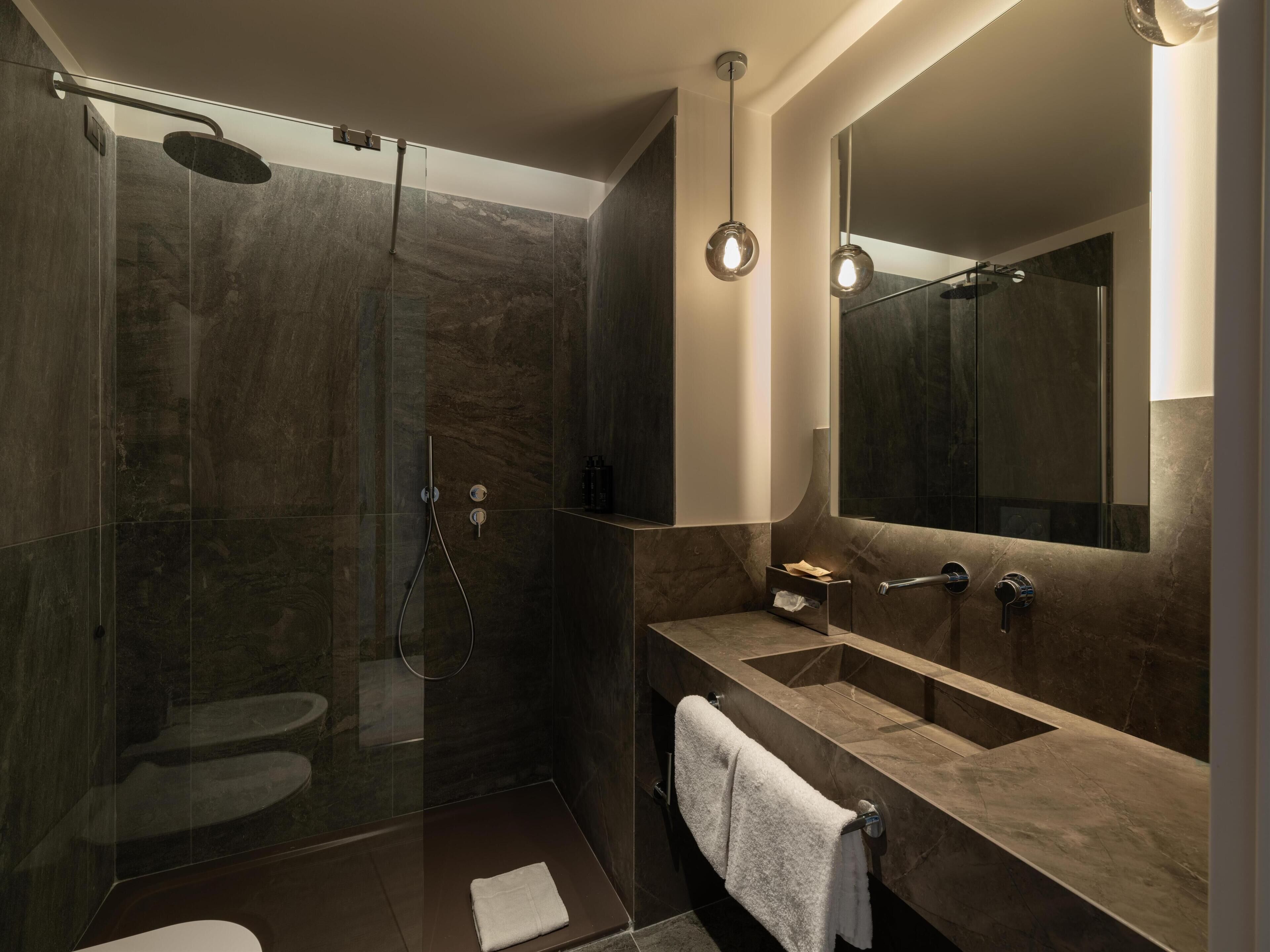 A modern bathroom with a glass-enclosed shower, a large mirror, and a marble countertop.
