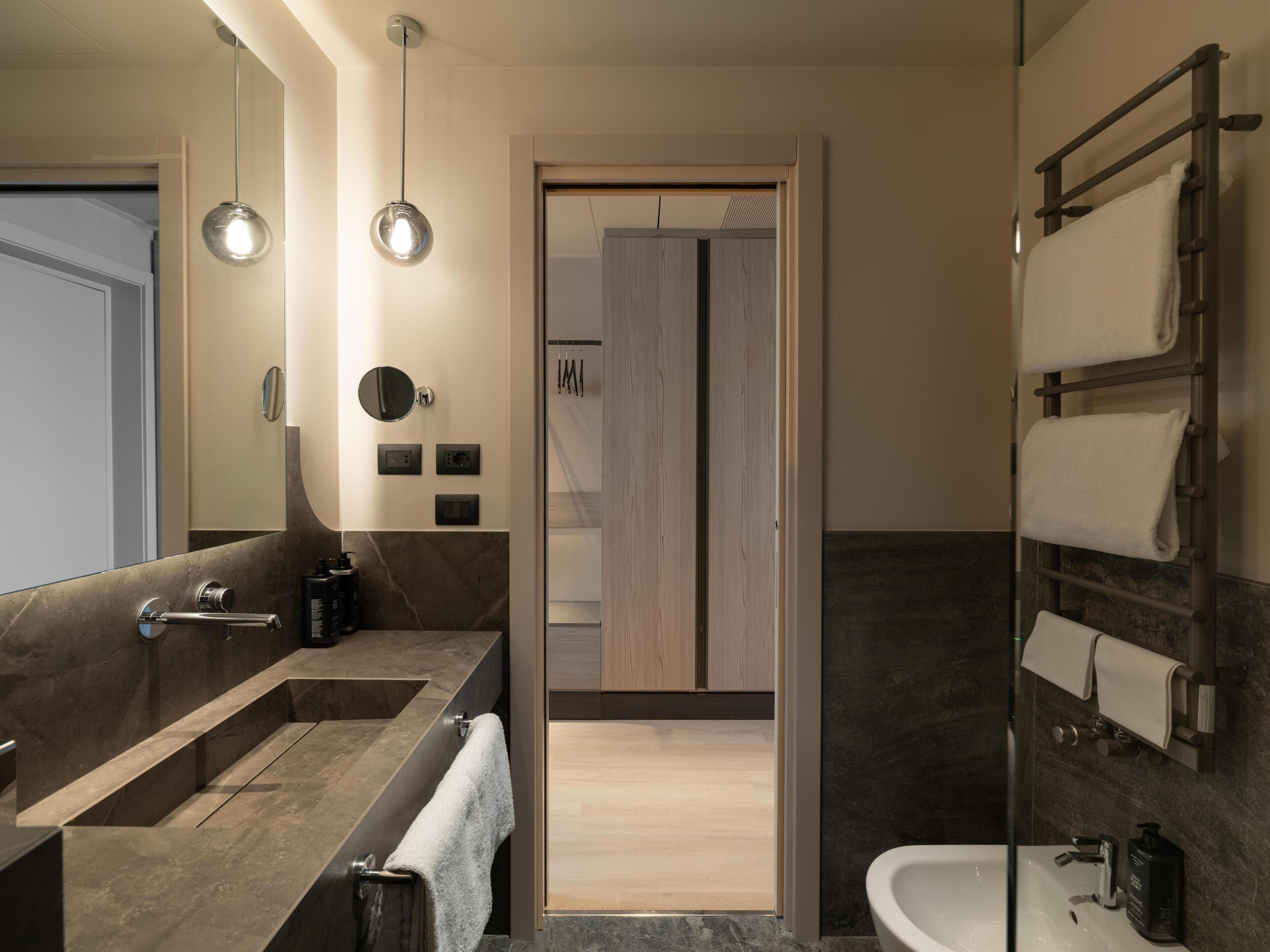 A modern bathroom with a double sink, a mirror, a towel rack, and a shower area.