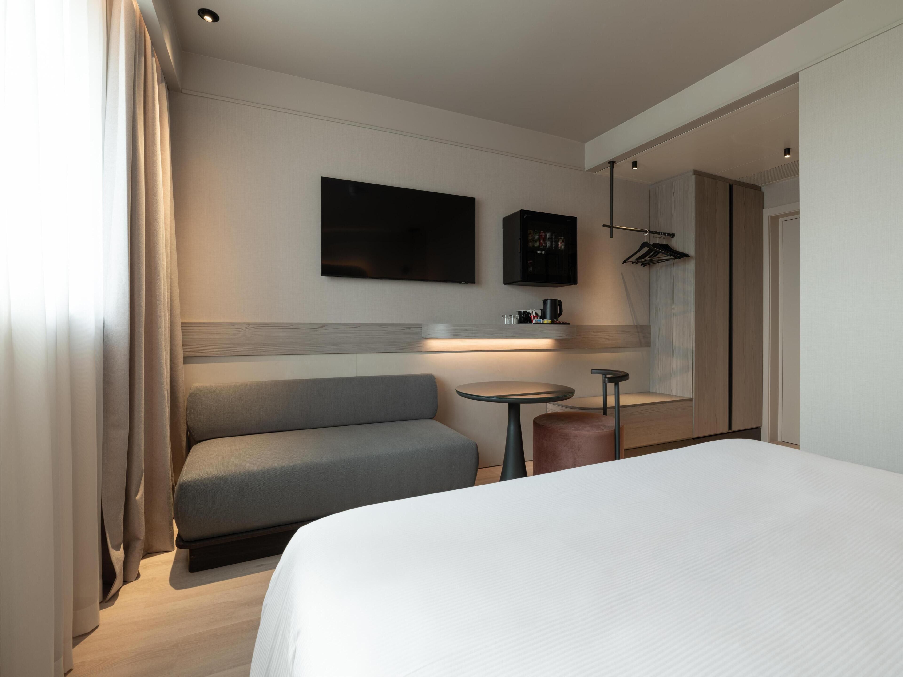 A hotel room with a bed, a seating area, a small table, a TV, and a mirror.