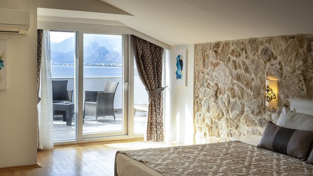 Un dormitorio con una cama grande, pared de piedra, vista al mar y un balcón con mobiliario de mimbre.